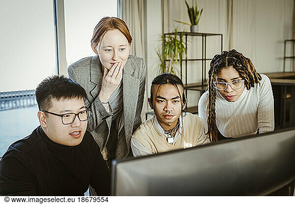 Multiracial programmers brainstorming over computer in creative office