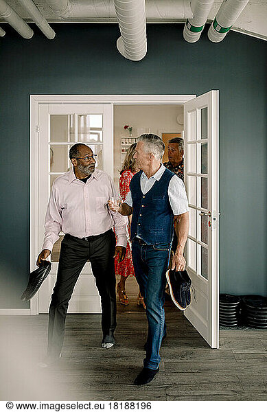 Multiracial senior men talking while carrying shoes and entering dance class