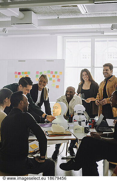 Multiracial students and professors discussing over social robot in innovation lab