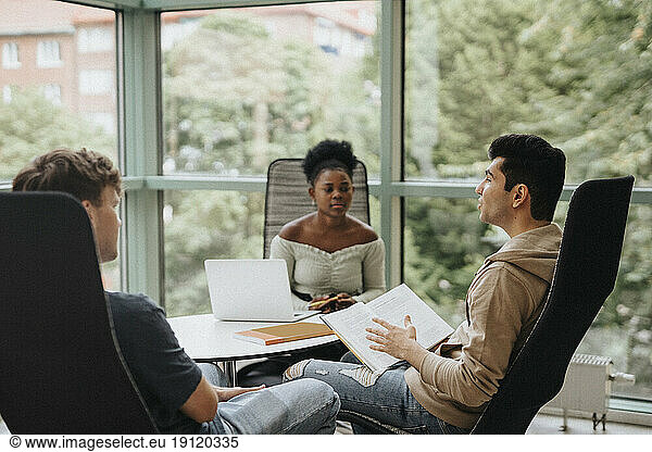 Multiracial students discussing while studying together in university