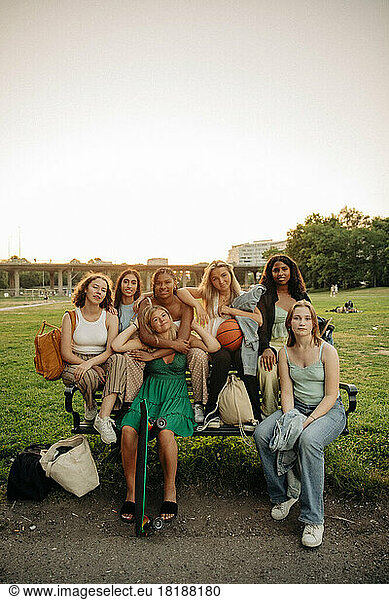 Multiracial teenage girls sitting on bench at park during sunset