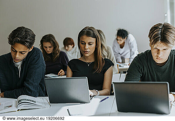 Multiracial teenage students studying at desk in classroom