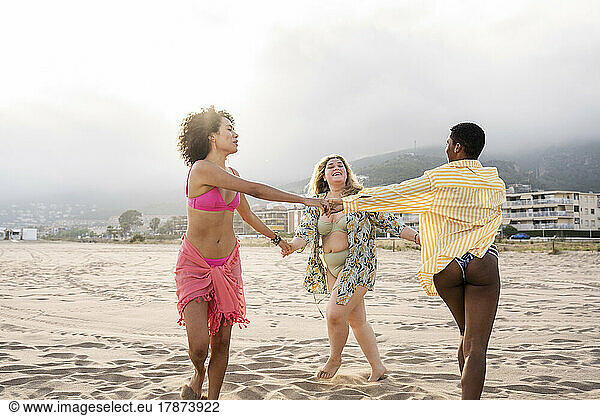 Multiracial women in swimwear playing ring around the rosy at beach
