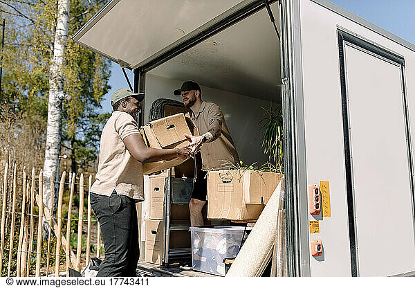 Multirassische Umzugshelfer entladen an einem sonnigen Tag Kartons vom Lastwagen