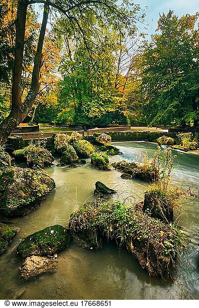 Munich English garden Englischer garten park and Eisbach river with artificial waterfall  Autumn colours on trees and leaves and flowing river  Munchen