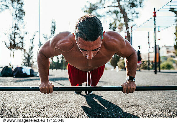 Muscled man doing a push-up on a barbell.