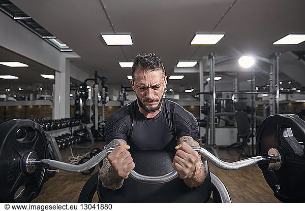 Muscular man lifting barbell while exercising at gym