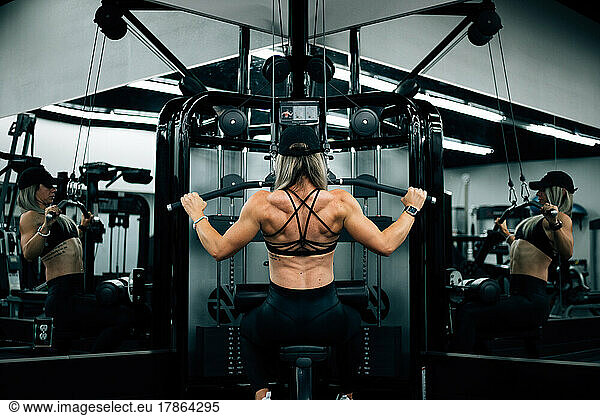 Muscular woman using machine at gym wearing black workout clothi