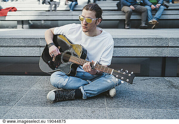 musician is performing outoor  sitting on the floor with people behind