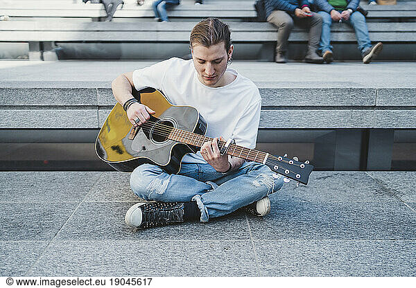 musician looking at the guitar sitting on the floor with people behind