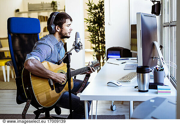 Musician singing while playing guitar at recording studio