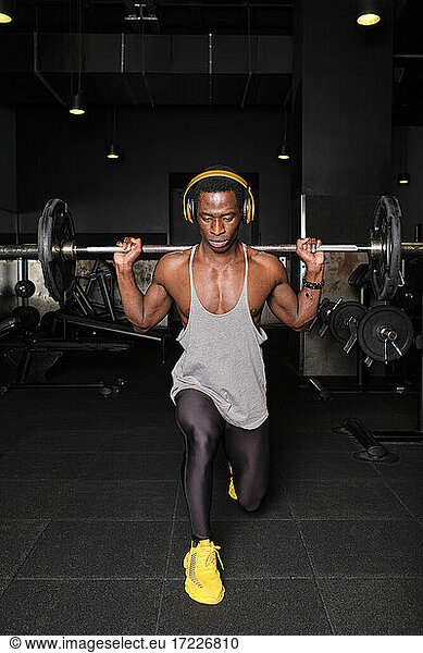Muskulöser Mann  der eine Langhantel hebt  während er im Fitnessstudio eine Ausfallübung macht