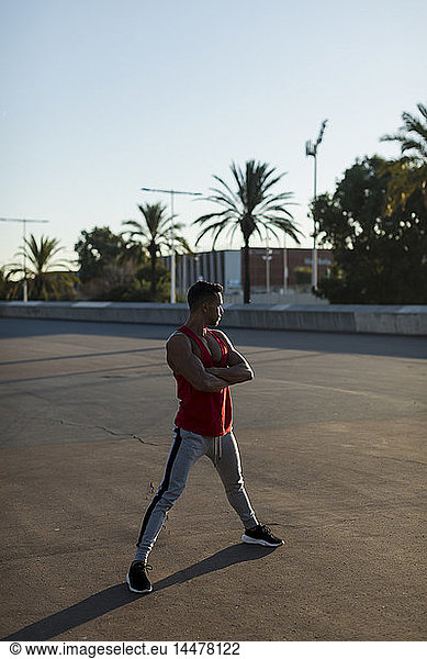 Muskulöser Mann steht mit verschränkten Armen auf dem Sportplatz