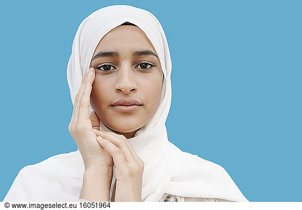 Muslimisches Mädchen berührt Gesicht vor blauem Hintergrund