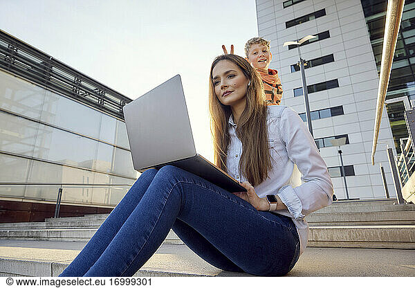 Mutter arbeitet am Laptop  während ihr Sohn im Hintergrund auf den Stufen steht