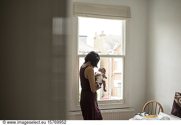 Mutter hält unschuldigen neugeborenen Jungen am Fenster