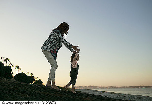 Mutter hilft Tochter bei Strandspaziergängen bei klarem Himmel
