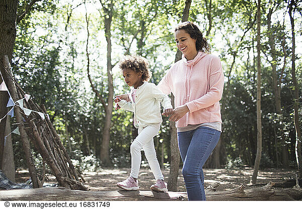 Mutter hilft Tochter gehen auf gefallenen Stamm in sonnigen Wald