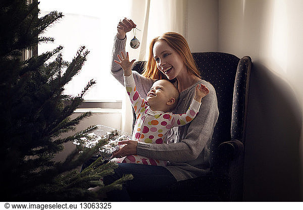 Mutter mit Tochter  die zu Hause auf einem Sessel sitzend den Weihnachtsschmuck ausbreitet
