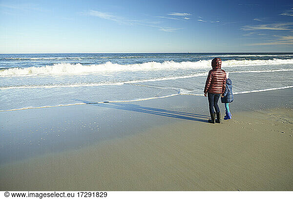 Mutter mit Tochter schaut am Strand stehend auf den Horizont