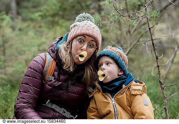 Mutter und Sohn machen beim Wandern im Winter beim Essen alberne Gesichter