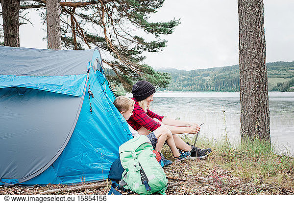 Mutter und Sohn sitzen in einem Zelt und binden Schnürsenkel und lächeln beim Camping