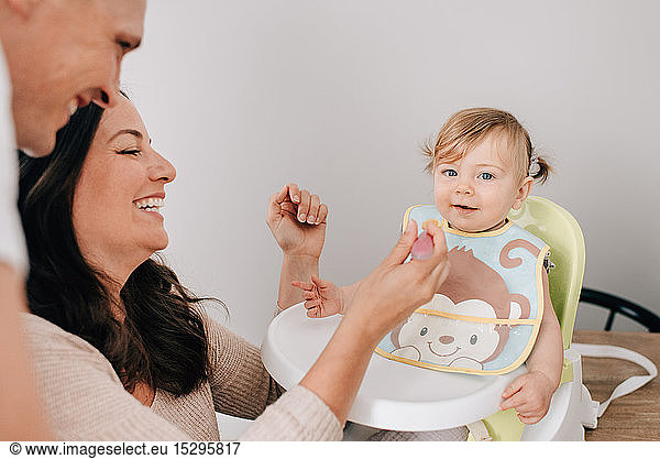 Mutter und Vater beim Füttern einer kleinen Tochter im Kindersitz  Porträt