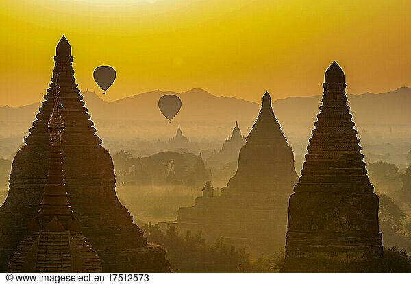 Myanmar  Mandalay Region  Bagan  Hot air balloons flying over ancient stupas at foggy dusk