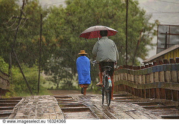 Myanmar  people on footbridge in monsoon rainfall