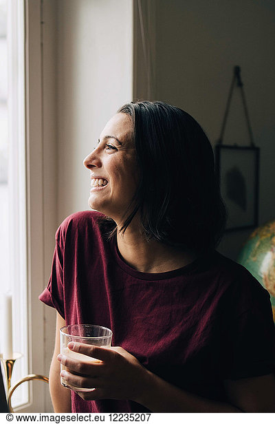 Nachdenklich lächelnde Frau beim Tee beim Blick durchs Fenster