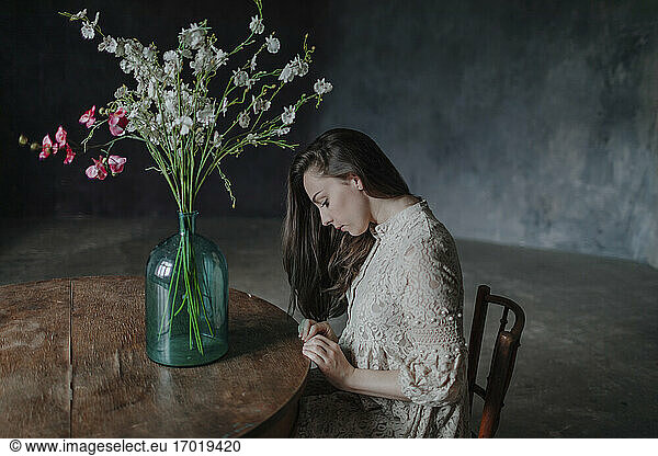 Nachdenkliche Frau mit Blumenvase auf dem Tisch