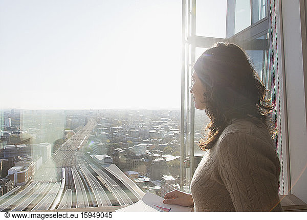 Nachdenkliche Geschäftsfrau am sonnigen Fenster mit Blick auf die Stadt