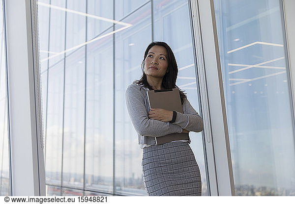 Nachdenkliche Geschäftsfrau hält digitales Tablet am Hochhausfenster