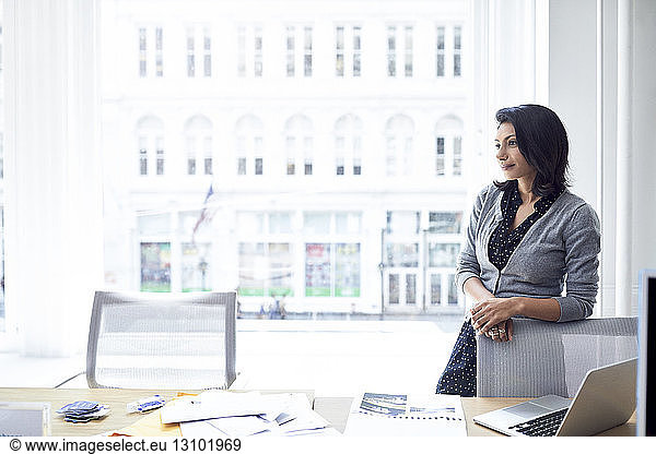 Nachdenkliche Geschäftsfrau schaut weg  während sie im Amt an einem Fenster steht