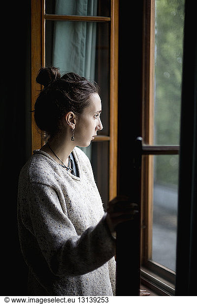 Nachdenkliche junge Frau  die zu Hause durch das Fenster schaut