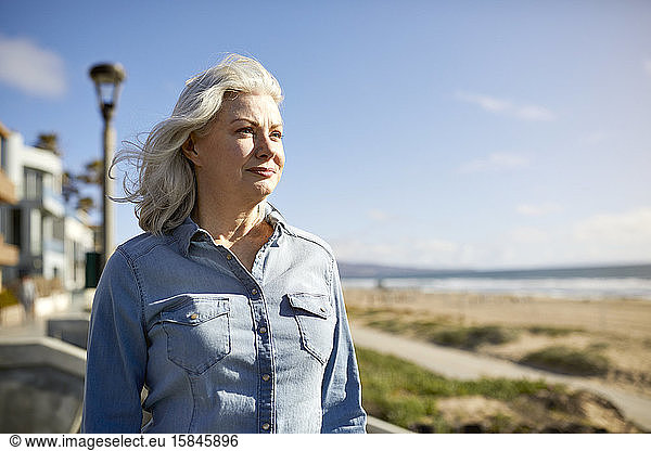 Nachdenkliche ältere Frau steht am Strand von Manhattan am sonnigen Tag am Himmel