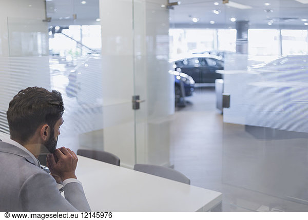 Nachdenklicher Autoverkäufer sitzt in Erwartung im Autohausbüro