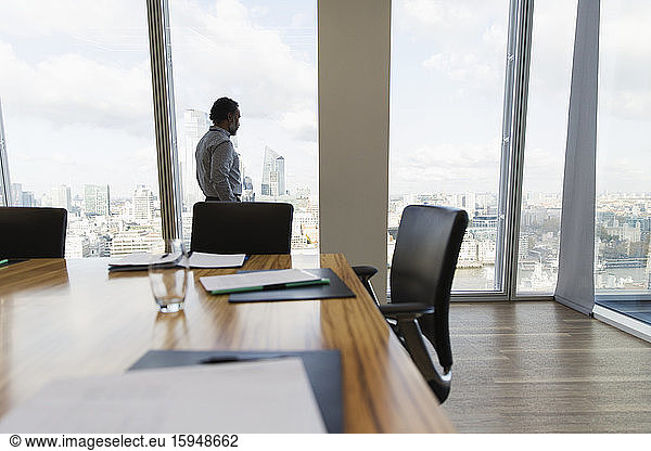 Nachdenklicher Geschäftsmann betrachtet Stadtbild am Fenster des Konferenzraums
