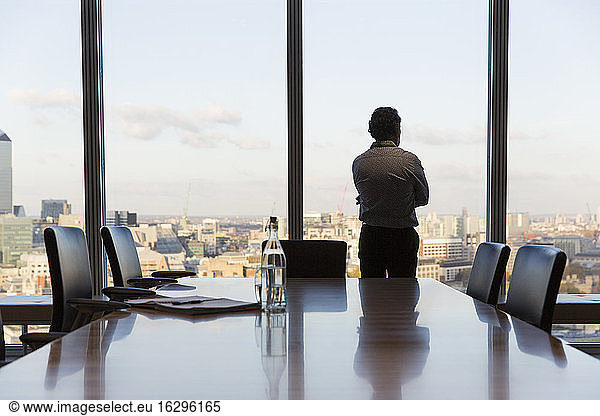 Nachdenklicher Geschäftsmann schaut aus dem Fenster eines städtischen Konferenzraums