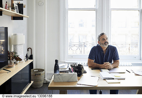 Nachdenklicher Geschäftsmann sitzt am Schreibtisch im Kreativbüro