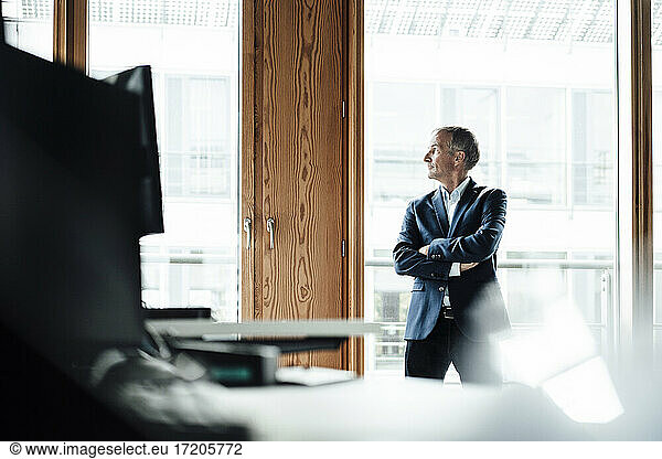 Nachdenklicher männlicher Unternehmer  der durch das Fenster schaut  während er am Fenster steht