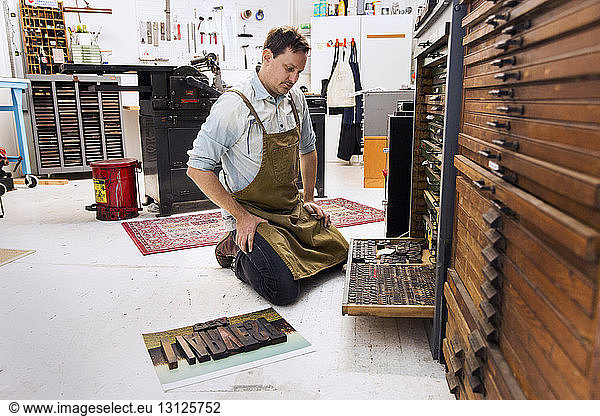 Nachdenklicher Mann betrachtet hölzerne Alphabete in der Druckerpresse