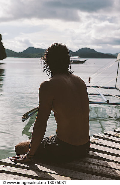 Nachdenklicher Mann ohne Hemd sitzt auf einem Steg über dem Meer