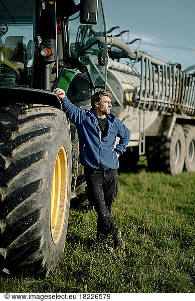 Nachdenklicher reifer Landwirt  der an einem sonnigen Tag auf einem Bauernhof am Traktor steht