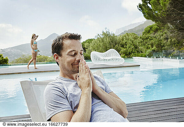 Nachdenklicher reifer Mann sitzt am Swimmingpool
