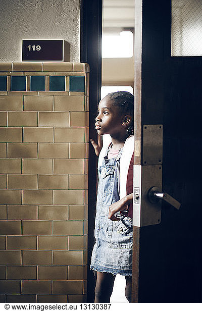 Nachdenkliches Schulmädchen steht an der Tür des Klassenzimmers