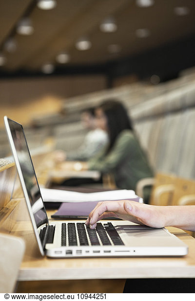 Nahaufnahme der menschlichen Handschrift auf der Laptop-Tastatur mit Personen im Hintergrund im Auditorium
