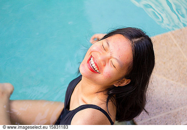 Nahaufnahme einer Asiatin  die lächelt  während sie in der Nähe des Pools sitzt