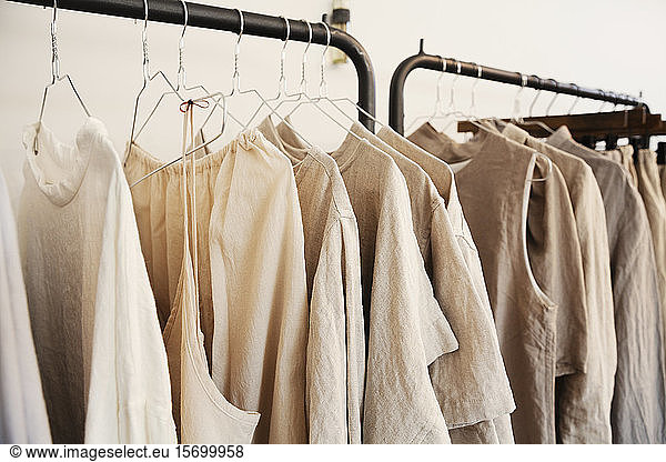 Nahaufnahme einer Auswahl von Kleidungsstücken in natürlichen Farben auf einer Schiene in einer Boutique.