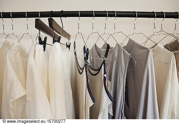 Nahaufnahme einer Auswahl von Kleidungsstücken in natürlichen Farben auf einer Schiene in einer Boutique.